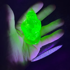 May include: A bright green glass figurine of a gorilla sitting with its arms crossed. The figurine is illuminated by a purple light.