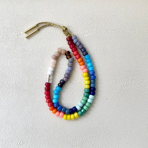 May include: A colorful beaded necklace with a rainbow of colors, including red, orange, yellow, green, blue, indigo, and violet. The necklace is made of small, round beads and has a gold clasp.
