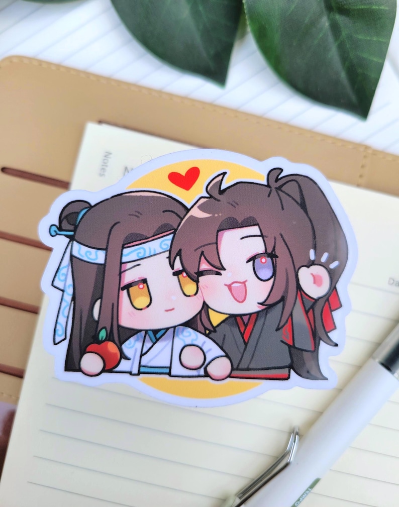 May include: A sticker depicting two cartoon figures with large eyes and smiling faces. One character is in a white and blue outfit, holding a red apple. The other is in a black and red outfit, winking and waving. A red heart is above them.