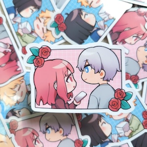 Può includere: Una collezione di adesivi in stile anime con coppie. Ogni adesivo mostra una coppia di personaggi dei cartoni animati con grandi occhi, che tengono in mano telefoni e sono circondati da rose. La tavolozza dei colori comprende rosa, blu e grigio.