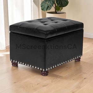 May include: A rectangular black ottoman with a tufted top and silver nailhead trim along the base. The piece features four dark brown rounded wooden feet and is marked with the text MScreeaktionsCA across the front side of the structure.