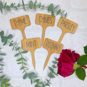 May include: Set of six wooden plant markers with black lettering. The markers are labelled "Thyme", "Chives", "Parsley", "Mint", "Rosemary", and "Sage".