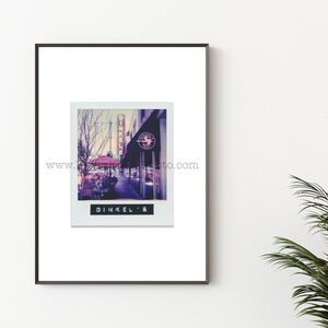 May include: A vintage-style photograph of a cafe called "Dinkel's" with a red awning and a sign with a bird logo. The cafe is located on a street with a tall building in the background.