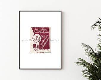 May include: A framed print featuring a vintage matchbox design. The matchbox has a cream background with burgundy text and illustrations. The text reads "South Shore's Newest Rendezvous" and "Continuous Entertainment". A woman is illustrated on the matchbox.