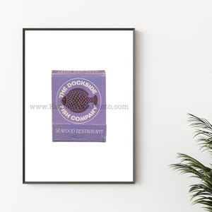 May include: A purple matchbox with a white circle and the text "The Dockside Fish Company Seafood Restaurant" printed on it. A black and white illustration of a fish is inside the circle.