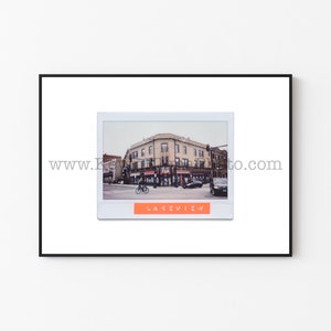 Puede incluir: Una foto Polaroid de estilo vintage de un edificio de ladrillo con un letrero que dice "Lakeview". El edificio está en una esquina de la calle con un coche y una bicicleta en primer plano.