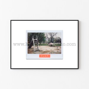 May include: A vintage Polaroid photo of a playground with a slide and a swing set. The photo is framed in a black frame and has the word "PLAY" printed on the bottom.