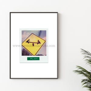 May include: Framed print featuring a Polaroid-style image of a yellow diamond-shaped road sign depicting a seesaw with two figures. The word "PLAY" is printed on a green rectangle below the image. The website address www.KevinKumaPhoto.com is printed on the image.