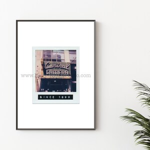 Könnte beinhalten: Ein gerahmter Druck mit einem Vintage-Bild im Polaroid-Stil des Central Camera-Geschäfts, mit dem Text "Central Camera" und "Since 1899". Das Bild ist vor einem weißen Hintergrund platziert.