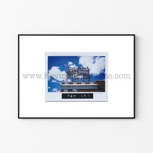 Può includere: Una fotografia vintage di un edificio con un grande cartello che recita "Columbia", con un cielo blu e nuvole bianche sullo sfondo. La foto è incorniciata da un bordo bianco e ha il testo "TRY IT!" stampato sotto l'immagine.