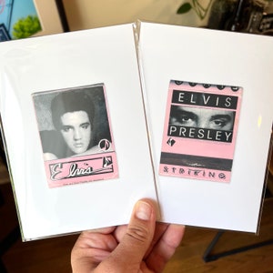 May include: Two white cardstock frames with pink and black matchbook covers. The left frame features a black and white photo of Elvis Presley with the text "Elvis" in a pink and black font. The right frame features a pink matchbook cover with the text "Elvis Presley" in black and the word "Striking" in black at the bottom.