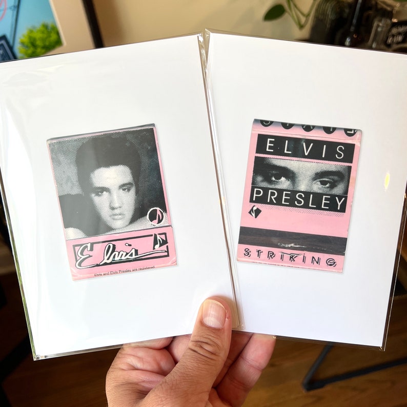 May include: Two white cardstock frames with pink and black matchbook covers. The left frame features a black and white photo of Elvis Presley with the text "Elvis" in a pink and black font. The right frame features a pink matchbook cover with the text "Elvis Presley" in black and the word "Striking" in black at the bottom.