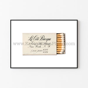 May include: A white matchbox with the text "La Cote Basque" in black cursive script. The address "85th Street, New York, N.Y." and phone number "(212) 688-6525" are also printed in black.
