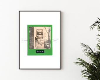 May include: A black and white photograph of a street scene with a sign that reads "Nuts on Clark" in a green frame. The sign is hanging from a building with a brick facade. The street is lined with trees and there are cars parked on the side of the road.