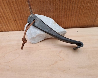 May include: A black metal bottle opener with a leather loop. The opener has a curved handle and a sharp edge for opening bottles.