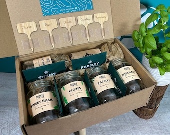 Könnte beinhalten: Ein Kräutergarten-Set aus Karton mit vier Glasgefäßen, die mit Sweet Basil, Chives, Parsley und Rosemary beschriftet sind. Das Set enthält fünf hölzerne Pflanzenstecker mit den Aufschriften Thyme, Basil, Chives, Parsley und Rosemary sowie braunes Papier.