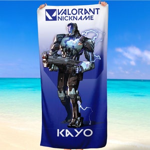 Könnte beinhalten: Ein blaues Strandtuch mit einem Valorant-Charakter, Kayo. Der Charakter ist ein Cyborg, der eine Waffe mit Blitzen hält. Der Text "VALORANT NICKNAME" befindet sich oben auf dem Handtuch und "KAYO" unten.