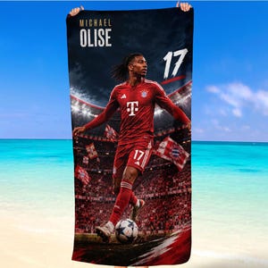 Könnte beinhalten: Ein rechteckiges Strandtuch mit einer Grafik des Fußballspielers Michael Olise im roten Trikot des FC Bayern München mit der Nummer 17. Das Design zeigt den Text MICHAEL OLISE und die Nummer 17 vor einem Stadionhintergrund mit einem Fußball.