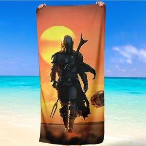 Könnte beinhalten: Ein Strandtuch mit der Silhouette einer mandalorianischen Figur in einer Wüstenlandschaft mit einer großen Sonne im Hintergrund.