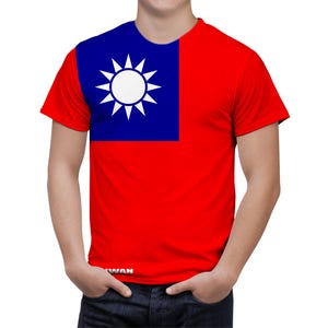 Puede incluir: Camiseta roja con la bandera de Taiwán. La parte superior de la camiseta es azul con un diseño de sol blanco. La parte inferior de la camiseta es roja. La persona lleva vaqueros azules.