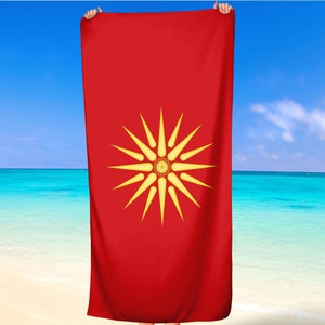 Könnte beinhalten: Ein rotes Strandtuch mit einem gelben Sonnenstrahlen-Design. Der Sonnenstrahlen hat 16 Strahlen und einen kleinen Kreis in der Mitte.