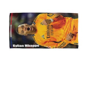 May include: A rectangular towel featuring a vibrant image of Kylian Mbapp&eacute; in an orange jersey. The towel has a colorful border with the text "Kylian Mbappe" at the bottom. The jersey has the text "Emirate FLY BETTER".