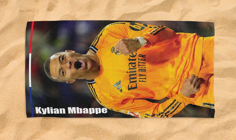 May include: A rectangular beach towel featuring a vibrant image of Kylian Mbapp&eacute; in a yellow soccer jersey. The towel has a red, white, and blue border and the text "Kylian Mbappe". The jersey has the text "Emirate FLY BITTER".