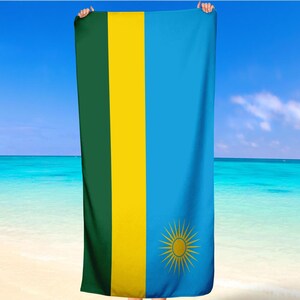 Può includere: Un asciugamano da spiaggia con la bandiera del Ruanda. L'asciugamano è verde, giallo e blu con un sole giallo al centro.