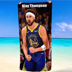 Peut inclure: Une serviette de plage avec une photo de Klay Thompson, joueur de basket-ball des Golden State Warriors. Il porte un maillot bleu et jaune avec le logo de l'équipe et les mots "Golden State Warriors".