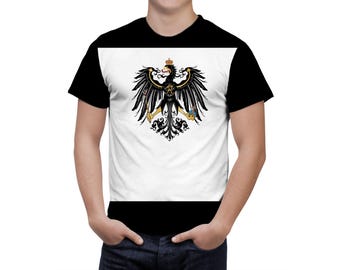 May include: Black and white t-shirt featuring a detailed graphic of a black eagle with a golden crown and accents. The eagle is centered on a white panel, with black sleeves and a black lower section.