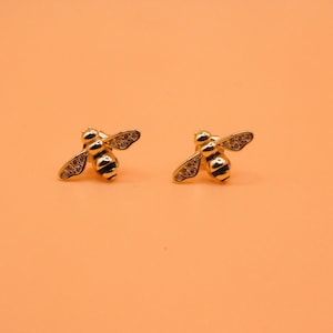 May include: A pair of gold bee stud earrings with clear crystal accents.