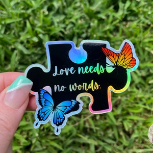 May include: A holographic sticker shaped like a puzzle piece with the text "Love needs no words."  Two butterflies, one blue and one orange, are on either side of the text.