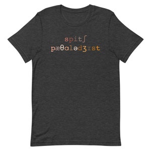 Op de afbeelding: Donker grijs t-shirt met een verloopontwerp dat "spit/pa00aled3ist" luidt.