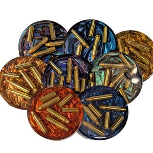 May include: Set of eight round coasters with a colorful, iridescent finish. Each coaster features a design of gold-colored bullet casings embedded in the resin.