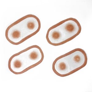 Puede incluir: Cuatro platos ovalados de cerámica blanca con borde marrón. Cada plato tiene dos círculos marrones en el centro.