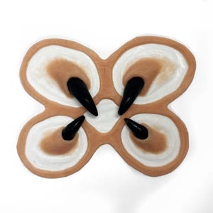 May include: Four black claw-like prosthetic nails are attached to a flesh-toned silicone base. The base is shaped like a four-leaf clover.