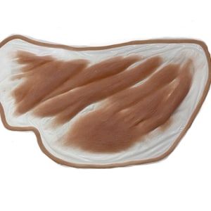 May include: A silicone prosthetic appliance featuring a realistic skin-toned surface with textured, raised brown areas resembling a wound or skin lesion. The piece has an irregular, organic shape with a thin, translucent edge for blending.