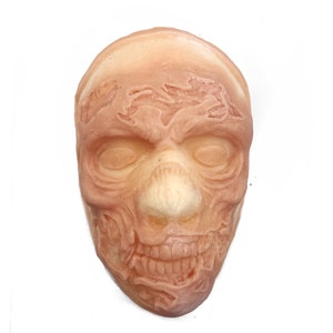 Peut inclure: Un masque en silicone réaliste et détaillé d'un visage humain avec une apparence vieillie et abîmée. Le masque est rose pâle et présente des rides, des lignes et une texture craquelée.