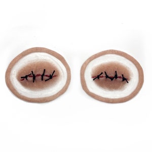 May include: Two round, flesh-colored, fake wound patches with black stitches and red thread.