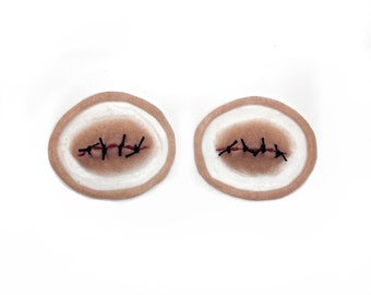 May include: Two round, flesh-colored, fake wound patches with black stitches and red thread.