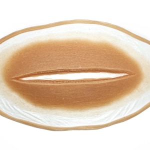 May include: A realistic-looking fake wound, made of a flexible material, with a long, thin cut in the center. The wound is a light brown color and has a slightly textured surface.