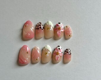 May include: A set of ten press-on nails featuring a pink and white color palette. The designs include pink swirls, black leopard print accents, white textured tips, and raised pink floral motifs with small gold metallic studs and pearls.