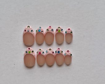 May include: A set of ten almond-shaped press-on nails featuring a light pink French tip design. Each nail is decorated with small, colorful star-shaped and round rhinestones along the cuticle line, accented by tiny white dots.