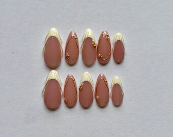 May include: A set of ten almond-shaped press-on nails featuring a nude base with cream-colored French tips. Some nails are adorned with thin gold wire accents and small gold beads, creating a delicate and refined look for a manicure set.