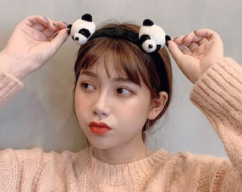 May include: Black headband with two plush panda bear ears. The headband is worn by a person with brown hair.