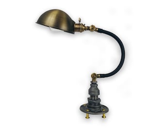 May include: A brass and black industrial style desk lamp with a flexible gooseneck arm and a dome-shaped shade. The lamp has a unique base made from pipe fittings.