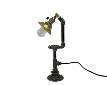 May include: A black metal table lamp with a gold-colored shade and a black cord. The lamp is made of industrial pipe fittings.
