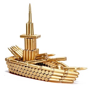 May include: A handcrafted sculpture of a ship constructed from numerous brass-colored bullet casings. The vessel features a tall central structure and multiple protruding "cannons" made from the same materials. The overall design is detailed and intricate.