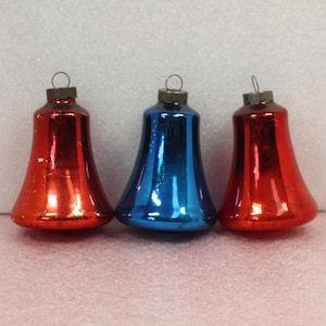 May include: Three vintage bell-shaped Christmas ornaments. Two are red, and one is blue. Each ornament has a metal cap with a loop for hanging. The ornaments are made of glass and have a shiny, reflective surface.