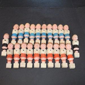 May include: A set of 20 vintage plastic foosball players. The players are in various poses, with some wearing blue and white uniforms and others wearing red and white uniforms. The players are all standing on white bases.